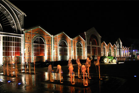 photo représentant le bâtiment, en brique, sous les lumières de la nuit, avec des jets d'eau décorant l'entrée