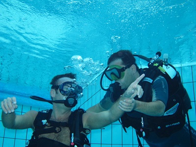 2 hommes font de la plongée dans une piscine, on ne voit pas lequel des 2 est en situation de handicap, mais l'un tient le bras de l'autre.